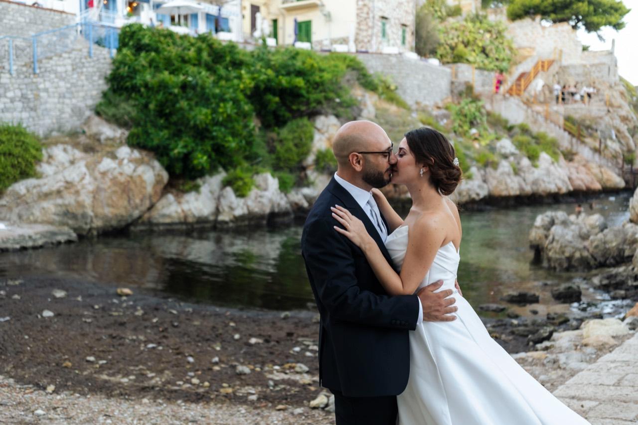 Gli sposi si baciano nella cala rocciosa.