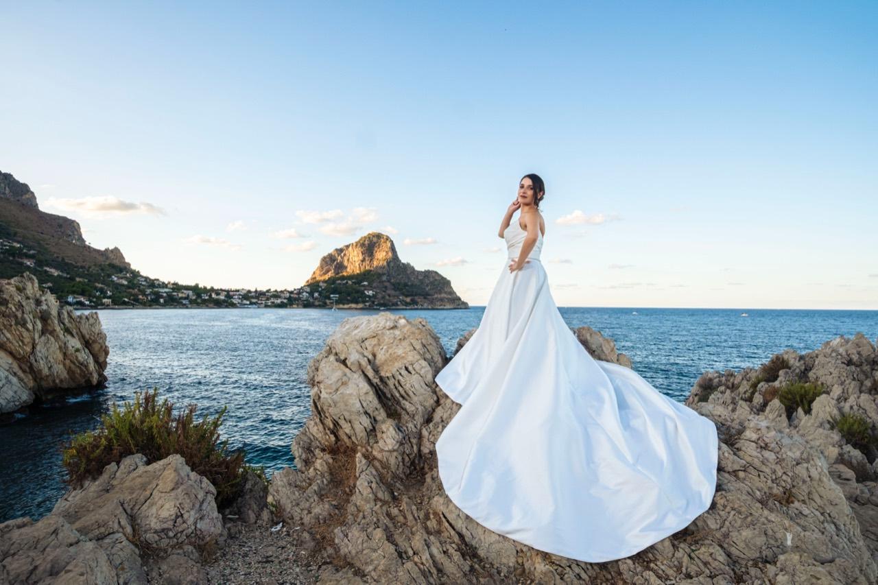 La sposa sulle rocce con il suo abito bianco e il mare sullo sfondo.
